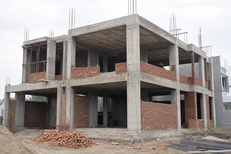 Unfinished reinforced-concrete house frame with red-brick masonry infill at the grey-structure stage